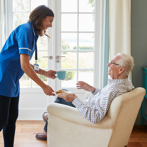 caregiver serving tea and snacks to elderly man in comfortable chair enjoying quality time together indoors with a warm atmosphere promoting companionship and healthy living 2 seniors