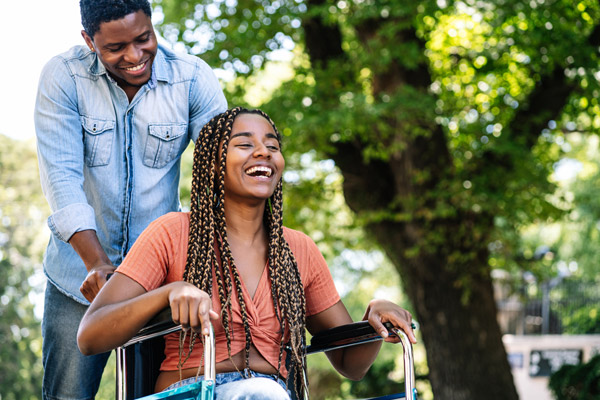 happy woman in wheelchair being pushed by smiling man in sunny park with trees joy laughter connection wheelchair accessibility friendship